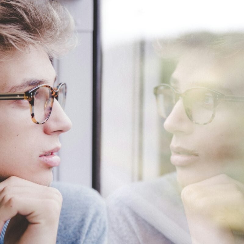 a man wearing glasses looking out a window