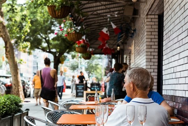 people dining outside restaurant near car parks under trees
