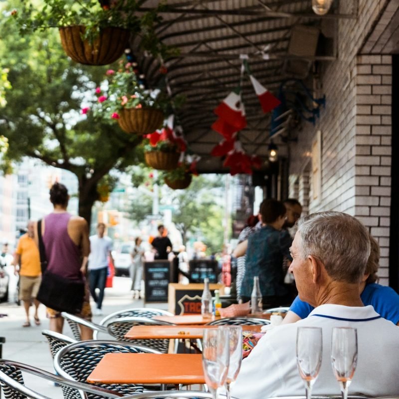 people dining outside restaurant near car parks under trees