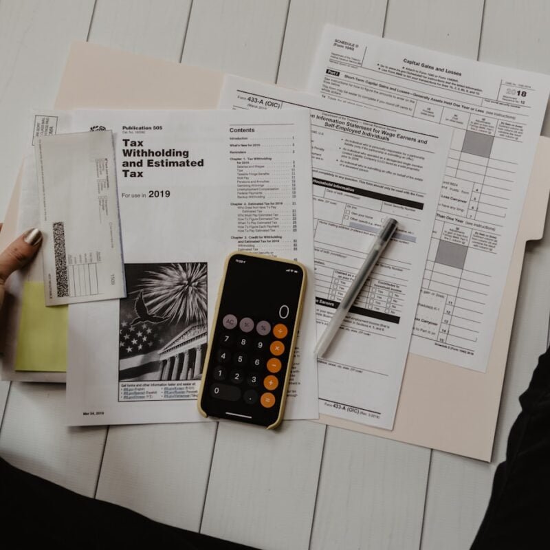 person holding paper near pen and calculator