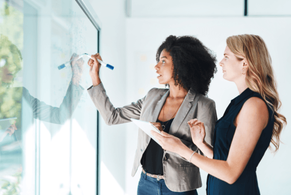 Shot of two businesswomen brainstorming with notes on a glass wall in an office