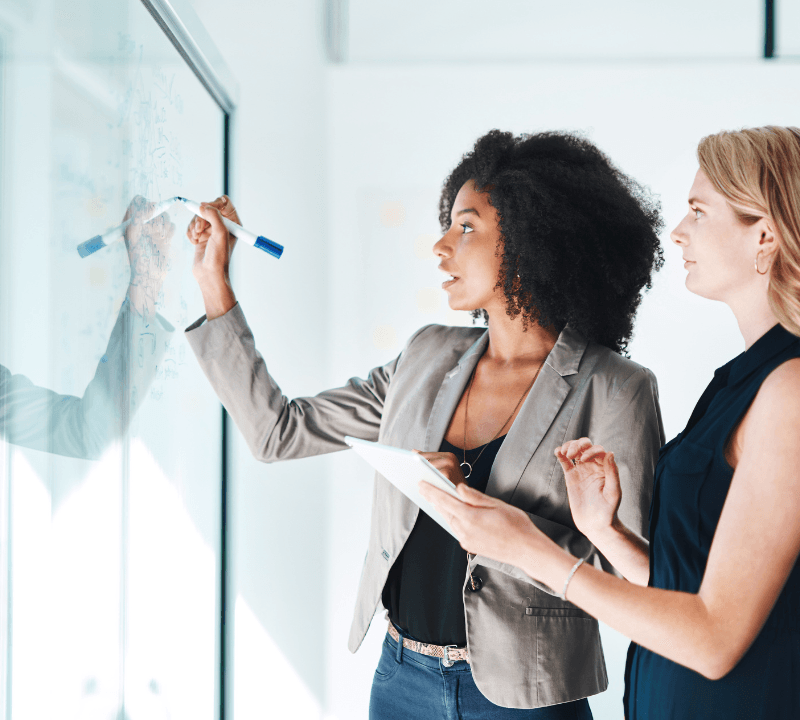 Shot of two businesswomen brainstorming with notes on a glass wall in an office