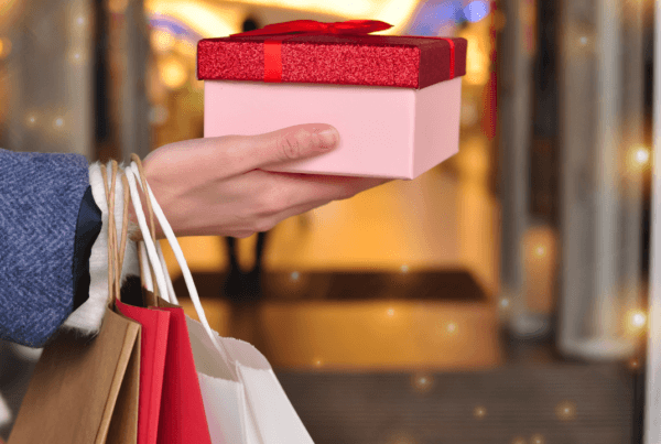 Customer’s hand holding red and white shopping bags in mall, copy space.