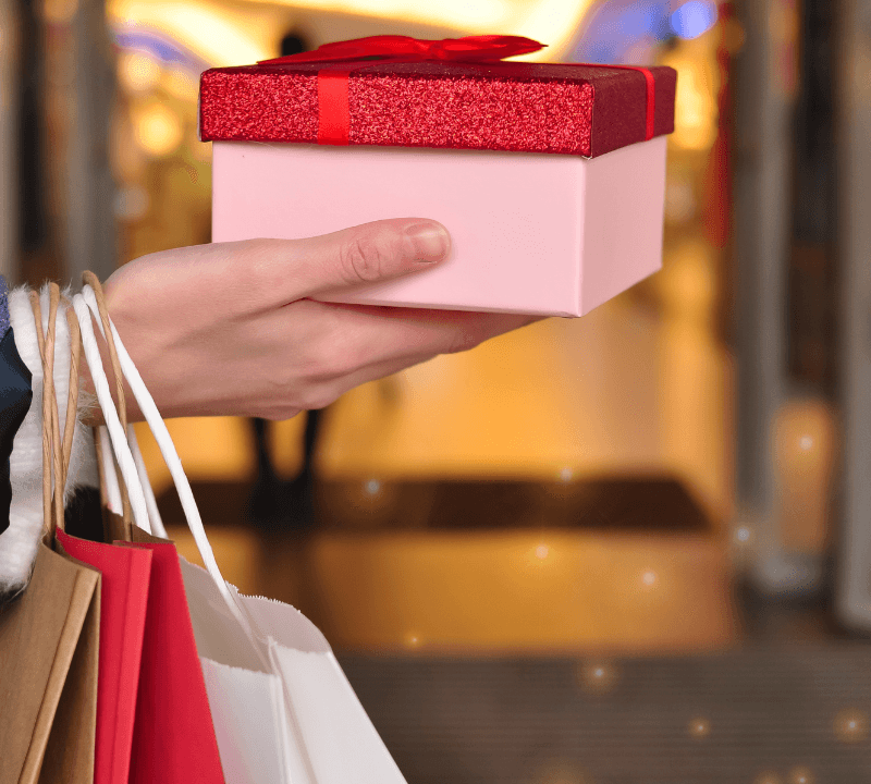 Customer’s hand holding red and white shopping bags in mall, copy space.