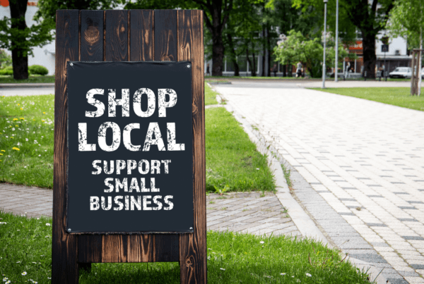 Shop local. Support small businesses. Wooden billboard on the street, sunny day.