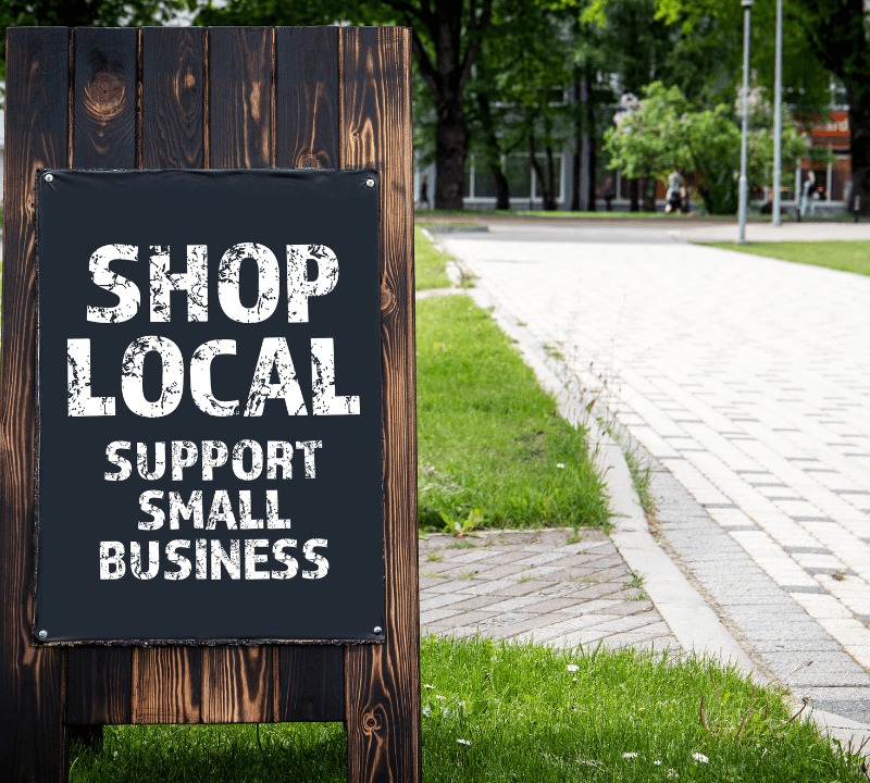 Shop local. Support small businesses. Wooden billboard on the street, sunny day.