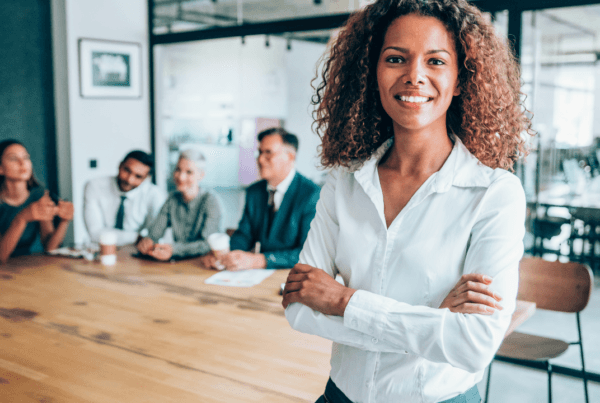 Shot of a beautiful African-american businesswoman standing with her arms crossed in front of her team in board room.