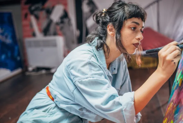 Young woman painter painting while sitting on the floor in studio.