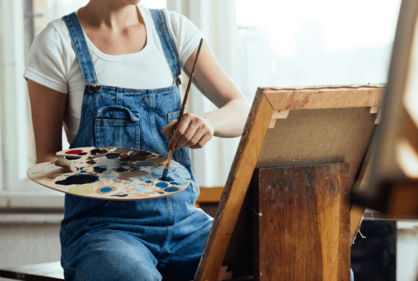 Young woman holding a color palette and painting on canvas in a studio.