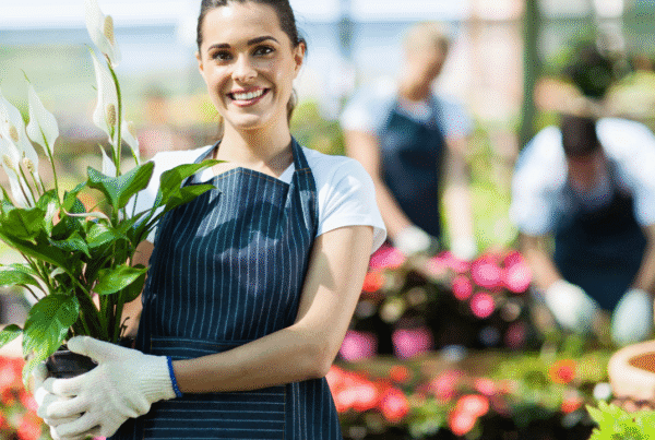 Happy female nursery owner with pot of flowers inside greenhouse.