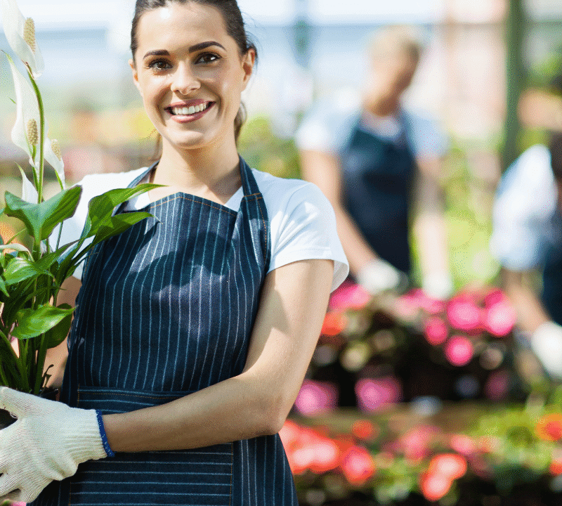 Happy female nursery owner with pot of flowers inside greenhouse.