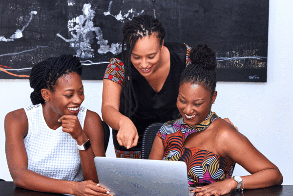 Three beautiful black women at a kitchen table looking at a laptop.