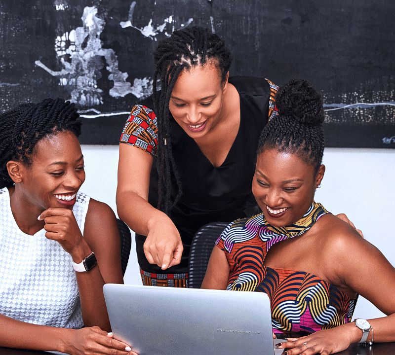 Three beautiful black women at a kitchen table looking at a laptop.