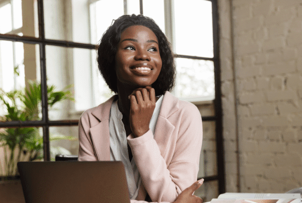 Confident smiling attractive young African woman entrepreneur working on laptop computer while sitting at the office desk