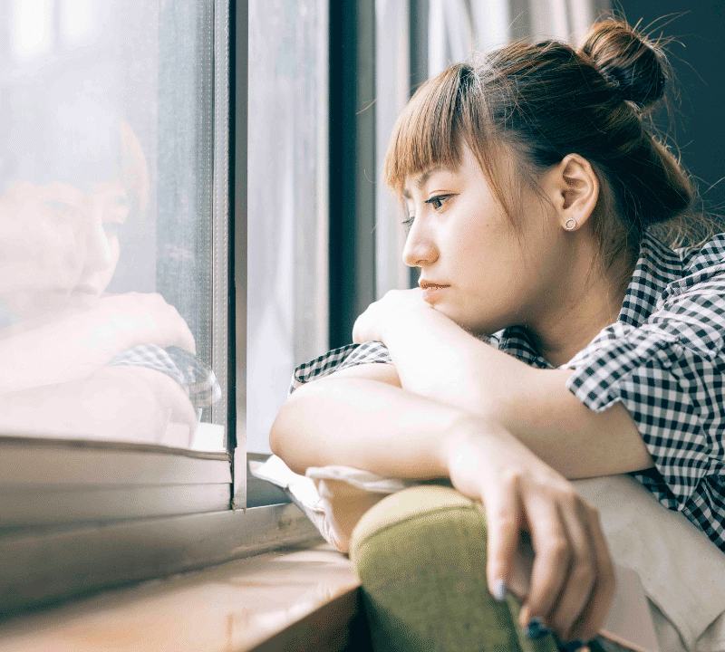 Young woman looking out of window looking lonely.