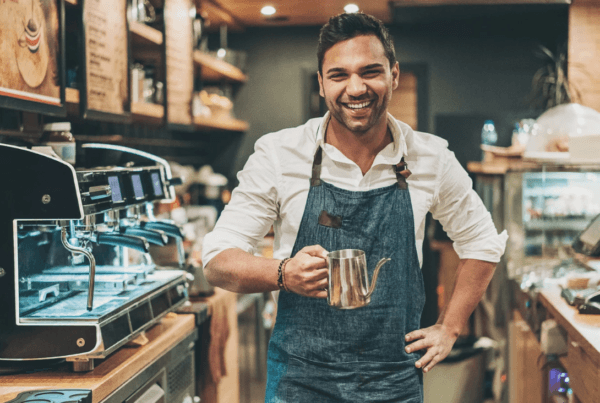 Smiling male barista holding a teapot in a coffee shop.