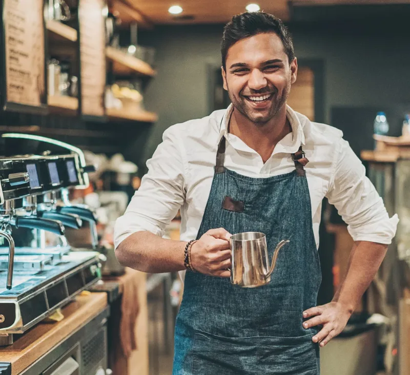 Smiling male barista holding a teapot in a coffee shop.