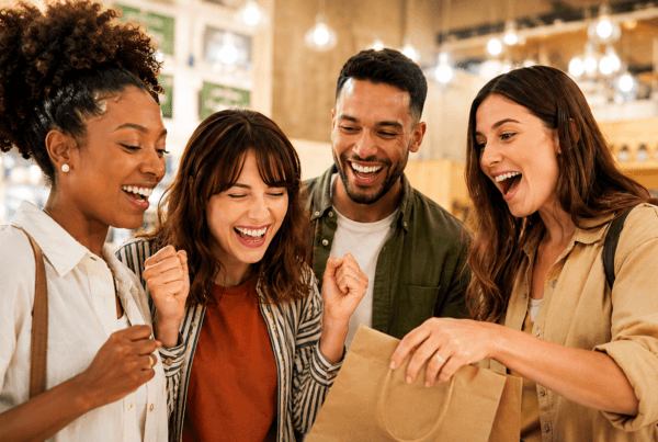 Four happy customers gather around a shopping bag in a warm, welcoming retail store, smiling and celebrating a purchase together. The bright, inviting atmosphere and joyful expressions convey a positive customer experience, strong relationships, and the excitement of discovering something special.